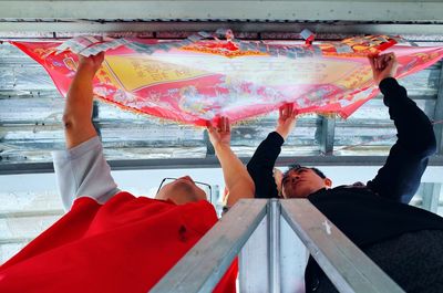 Men adjusting red textile on ceiling