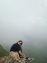 Portrait of woman sitting on cliff during foggy weather