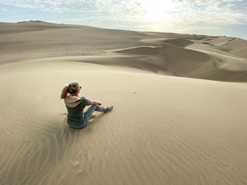 Rear view of woman sitting on sand dune