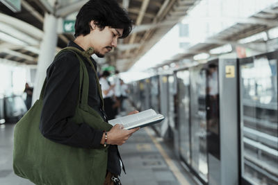 Side view of man reading book at railroad station