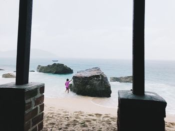 Rear view of people on rock at beach against sky