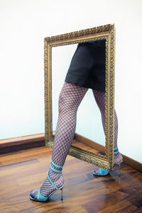 Low section of woman standing on hardwood floor against wall