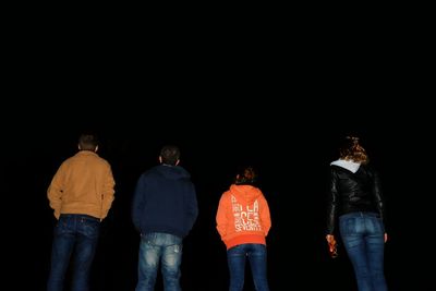Rear view of people standing against black background