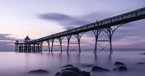 Bridge over river against sky at sunset