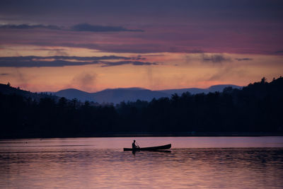 Silhouette person in boat on lake against sky during sunset