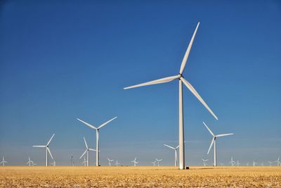 Wind turbines on field against blue sky