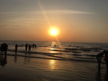 Silhouette people standing on beach against sky during sunset