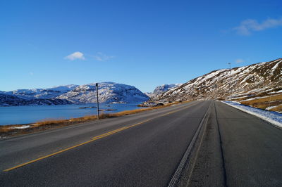 Road amidst snowcapped mountains against blue sky