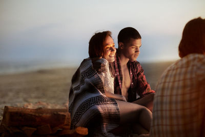 Happy woman sitting with man on beach at dusk