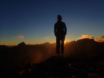 Rear view of silhouette man standing on mountain against sky