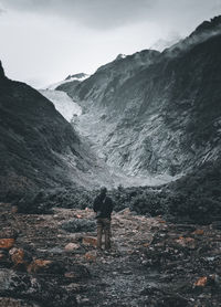 Rear view of man standing on mountain against sky