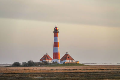 Lighthouse on field by building against sky