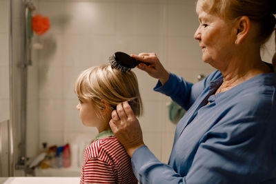 Side view senior woman combing hair of grandson in bathroom at home