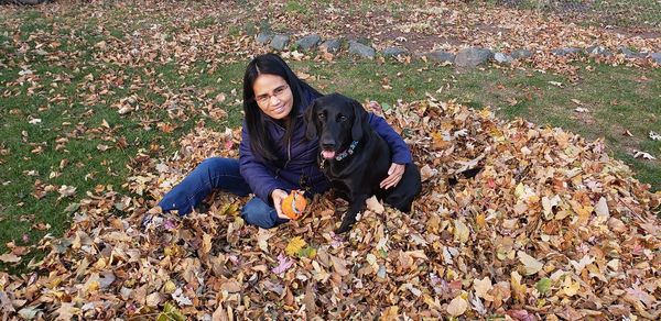 Portrait of woman sitting with dog on fallen autumn leaves at park