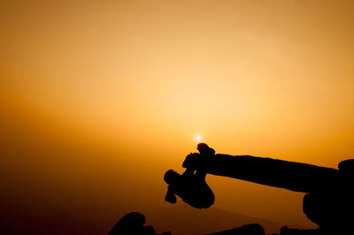 Silhouette person climbing on cliff against sky during sunset