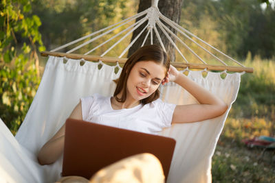 Young woman using mobile phone while sitting on hammock