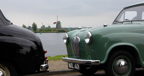 Vintage cars parked by lake against sky