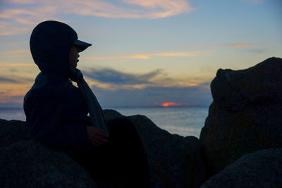 Man standing on rock by sea against sky during sunset