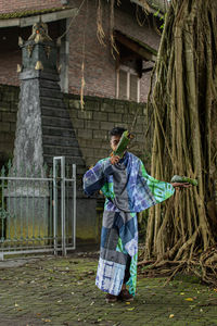 A man in patchwork dress standing with leaves on both of his hands