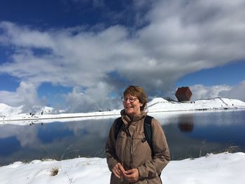 Smiling mature woman standing on snow against lake