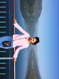 Portrait of smiling woman standing on bridge against clear sky