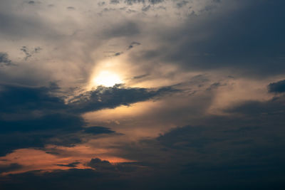 Low angle view of sunlight streaming through clouds during sunset