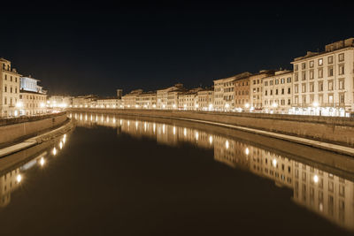 Reflection of illuminated buildings in river against sky at night