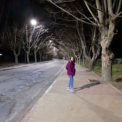 Full length rear view of woman standing on footpath at night