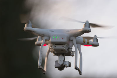 Drone quadcopter hovering in front of trees and blue sky, selective focus blurs the background