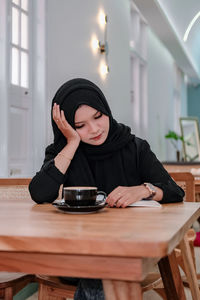 Young woman using mobile phone while sitting on table