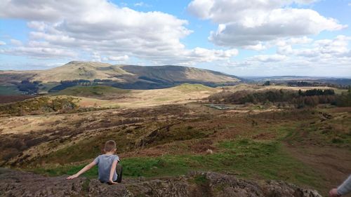 Full length of boy sitting on rock formation against cloudy sky