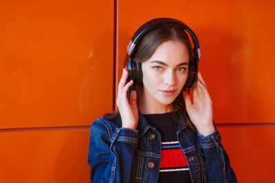Portrait happy smiling young woman with headphones listening to music on orange