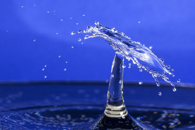 Close-up of drop splashing on water against blue background