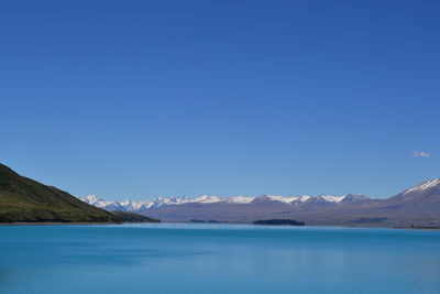 Scenic view of lake by mountains against clear blue sky