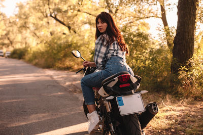 Portrait of woman riding motorcycle on road against trees