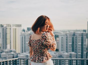 Beautiful young woman standing against buildings in city against sky