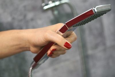 Close-up of woman holding shower faucet at bathroom