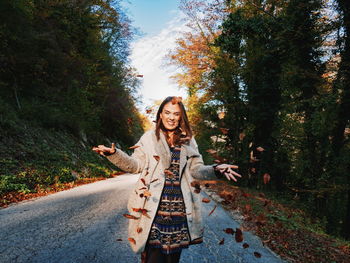 Portrait of smiling young woman on road against trees