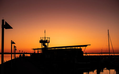 Silhouette pier over sea against orange sky