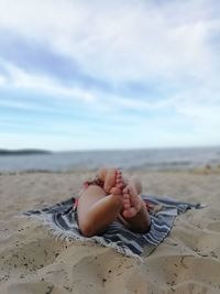 Low section of woman lying on sand at beach against sky