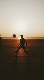 Silhouette man playing soccer at beach