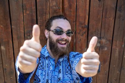 Young man gesturing while standing against wooden wall