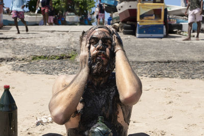 Man covered in oil walking on the sandy beach with the sea in the background.