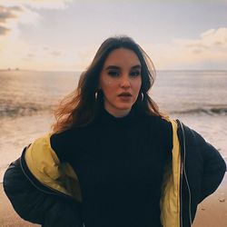 Portrait of young woman standing at beach against sky