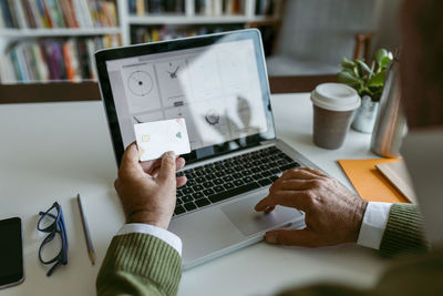 Human hand using credit card while working on laptop at home