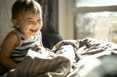 Cute baby laughing in duvet on bed at home