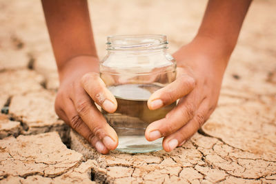 Cropped hands of person holding jar with water on cracked field