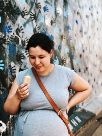 Pregnant woman having ice cream cone against wall