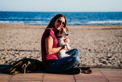 Woman sitting on beach by sea against sky