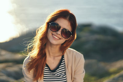 Portrait of smiling woman wearing sunglasses while standing against sea